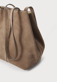 Bruine suède totebag met een zachte textuur, open bovenkant en lange leren hengsels, voorzien van contrasterende stiksels langs de randen.