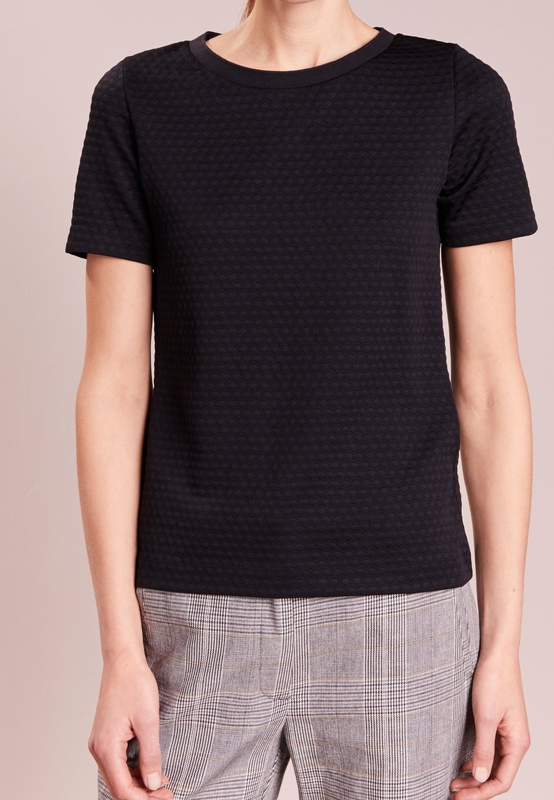 Camiseta negra de manga corta hecha de tejido texturizado con cuello redondo, combinada con pantalones de cuadros claros.