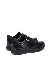 Zapatillas negras de cuero con un diseño elegante, que cuentan con una suela resistente, detalle de cremallera metálica y acentos marrones en el talón.