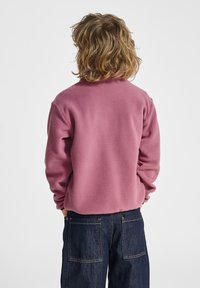 Roze fleece trui met een ronde halslijn, achterkant zichtbaar, gecombineerd met donkere spijkerbroek, met een losse pasvorm en zachte textuur.