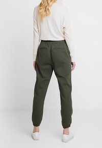 Donkergroene joggerbroek met een elastische tailleband, zijzakken en elastische boorden. Draag het met een witte lange mouwen top en witte schoenen.