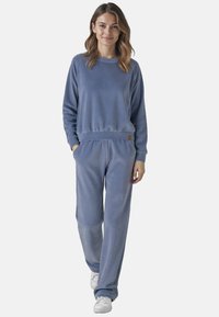 Modrý fleece set na relaxaci, který obsahuje svetr s kulatým výstřihem a kalhoty volného střihu. Oba kousky mají příjemný úplet a elastický pas s logem.