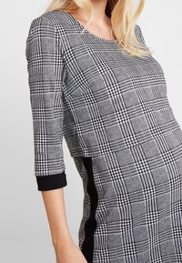 Svartvit rutmönstrad klänning med rundad halsringning, trekvartslånga ärmar med svarta manschetter och svarta paneldetaljer på sidorna.