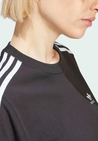 Svart bomullssweatshirt med hvit tre-stripesdesign på skuldrene og liten logo på brystet. Rund hals og myk tekstur.