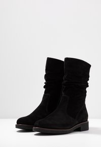 Bottines en suède noir avec un haut fluide, semelle en caoutchouc plate et coutures ton sur ton. Elles présentent une texture lisse et un design minimaliste.
