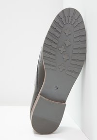 Semelle de chaussure en caoutchouc gris avec motif texturé, présentant des rainures horizontales et verticales, et une étiquette indiquant la taille 37.