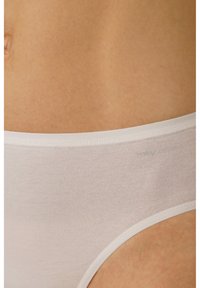 Slip in cotone bianco con superficie liscia, caratterizzato da una morbida vita elastica e dettagli di cucitura discreti. Posizionato su uno sfondo di tonalità della pelle.