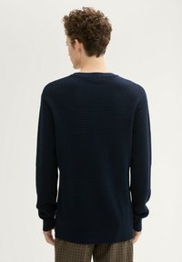 Granatowy sweter o fakturze z okrągłym dekoltem i długimi rękawami, z wzorem w kratkę. Materiał wydaje się miękki, z prążkowanymi mankietami i dołem.