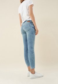 Blå denim skinny jeans med midjehöjd, med bakfickor och en läderlogotyp, ihop med en vit t-shirt och sneakers.