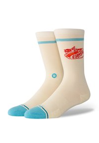 Cream-colored crew socks with blue accents, featuring a red "STANCE" logo and patterned ribbed cuffs. Light and soft fabric.
