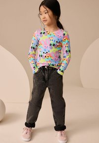 Langærmet, multicolor top med tegneserie dyremønstre; sort bukser i denim-look; lyserøde sneakers med hvide accenter; ensfarvet baggrund.