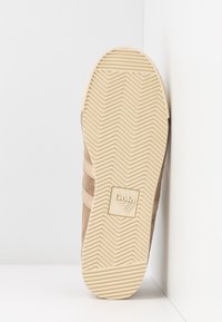 Semelle de sneaker en suède tan avec un motif en chevrons en caoutchouc beige, logo en relief et trois bandes d'accent sur le côté.