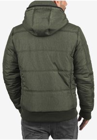 Giacca puffer verde oliva con cappuccio, realizzata in un tessuto testurizzato, con polsini a coste e un design trapuntato, visibile dalla parte posteriore.