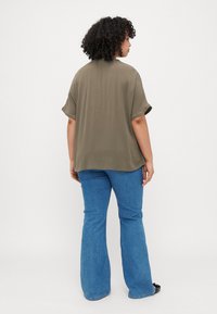 Olive green short-sleeve blouse with a loose fit, rounded hem, paired with blue flared denim jeans. Smooth texture, casual design.