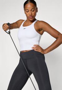 Biely športový crop top s dizajnom na pretekárov, kombinovaný s čiernymi vysoko pásovými legínami. Textúrovaná tkanina a priliehavý strih.