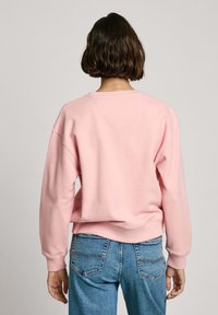 Sudadera de color rosa claro hecha de tela suave, con un ajuste relajado, cuello redondo y puños acanalados, combinada con jeans de mezclilla azul.