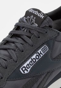 Šedé tenisky vyrobené z textilného a semišového materiálu, s logom Reebok, zosilnenými očkami a okrúhlymi šnúrkami v elegantnom, aerodynamickom dizajne.