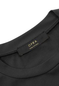 Czarna tkanina o gładkiej fakturze, z okrągłym dekoltem. Metka głosi "OPRA" w złotym, z napisem "Wyprodukowano w Polsce" poniżej.