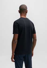 Černé bavlněné tričko s kulatým výstřihem, krátkými rukávy a hladkým povrchem. Mírně fitted design, pohled zezadu.