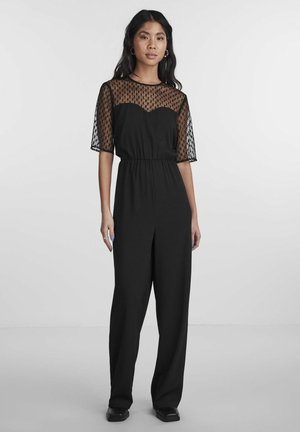 Combinaison noire avec des manches courtes en tulle transparent à pois et une taille ajustée. Présente des jambes larges et une texture de tissu lisse.