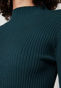 Ribattu turtleneck neule tumma teal väri. Ominaisuuksia ovat korkea kaulus, teksturoitu neulekuvio ja tiukka siluetti. Valmistettu pehmeästä, joustavasta materiaalista.
