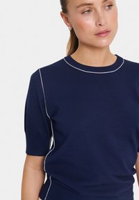 Top en maille bleu marine à manches courtes, avec une bordure contrastante blanche le long de l'encolure et des coutures latérales, texture lisse, design ajusté.