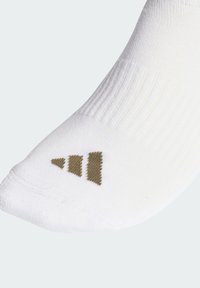 Bílá sportovní ponožka s žebrovanou strukturou, zdobená zlatým trojúhelníkovým logem poblíž špičky. Nylonová směs zajišťuje pružnost a pohodlí.