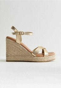 Sandale compensée métallique dorée avec une semelle en jute de style espadrille, dotée de deux brides croisées et d'une sangle de cheville réglable.