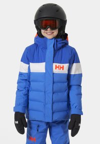 Modrá izolovaná lyžařská bunda s kontrastními bílými pruhy a oranžovým logem, vybavená kapucí, zipovým uzávěrem a elastickými manžetami. Součástí jsou černé rukavice.