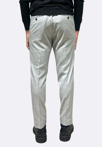 Pantaloni grigio chiaro su misura con tessuto strutturato, caratterizzati da doppie tasche posteriori con bottoni neri, abbinati a scarpe nere.