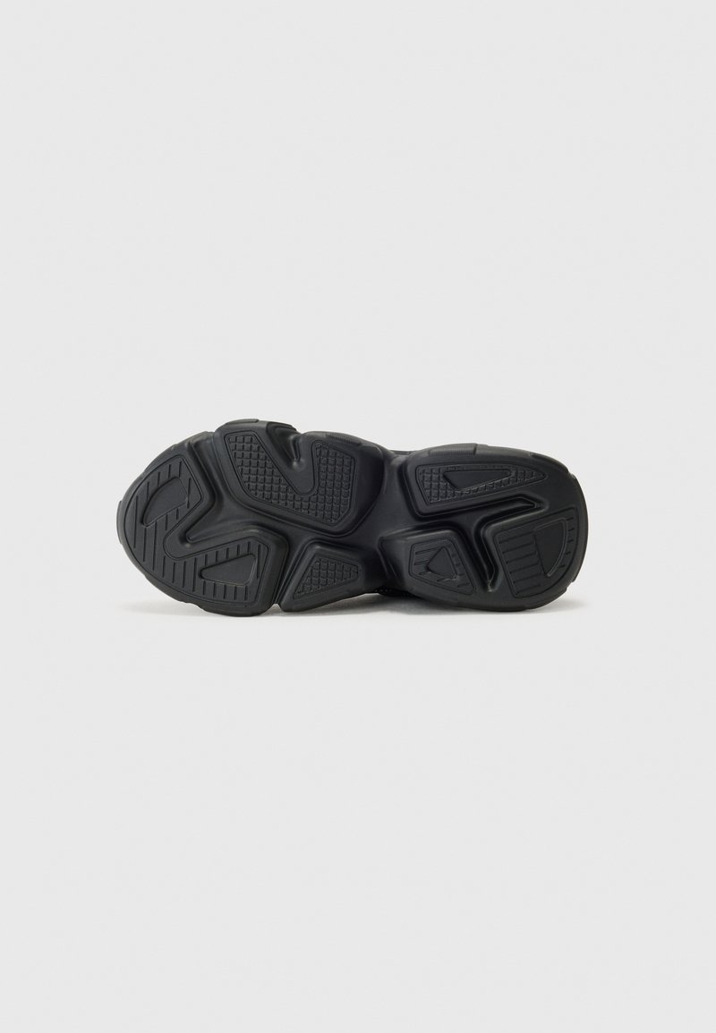 Semelle de sneaker noire avec une surface texturée comportant des motifs distincts, des crêtes et des découpes pour une meilleure traction et un soutien accru.