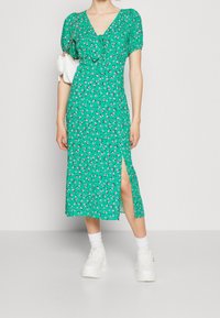 Zielona kwiatowa sukienka midi z bufkami i dekoltem w serek; posiada boczne rozcięcie. Połączona z białymi sneakersami na platformie i białą torbą.