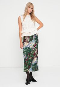 Hvit strukturert peplum-toppen kombinert med et langt grønt blomsterkjørt med et scenisk mønster, brukt med svarte strømpebukser og flate sko.