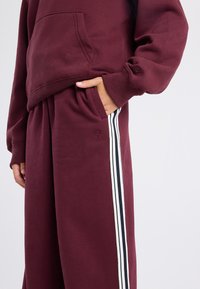 Maroon sweatshirt with a kangaroo pocket and matching maroon pants. Pants feature white and navy vertical stripes on the side.