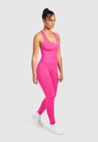 Figurpassande rosa bodysuit i stretchmaterial med rundad halsringning och racerback-design, kombinerad med vita sportskor.