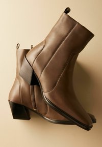 Bottines en cuir marron avec un bout carré, un talon effilé et un détail de fermeture éclair sur les côtés. Texture lisse avec de subtils accents de couture.