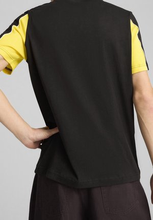 Svart och gul kortärmad skjorta med svart rygg och gula detaljer på ärmarna, tillverkad av slät tyg; minimalistisk design med söm-detaljer.