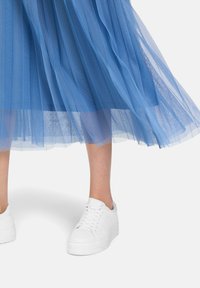 Gonna midi in tulle blu con texture a strati e tessuto trasparente, abbinata a sneaker bianche chunky. Focus sulla fluidità della gonna e sul colore vivace.