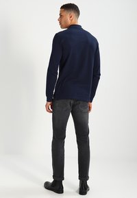 Marineblå langermet polo skjorte med rett snitt, kombinert med mørkegrå slim-fit jeans og svarte ankelstøvler. Glatt stoff og klassisk design.