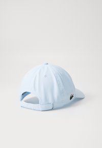 Boné de beisebol azul claro feito de tecido liso, com um logótipo bordado verde de um lado e uma fita ajustável na parte de trás.