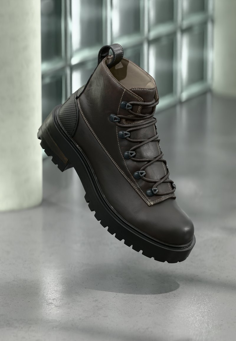 Botte de randonnée en cuir marron avec une tige haute, une semelle en caoutchouc robuste, des œillets en métal et des accents cousus. Comprend une languette de traction à l'arrière.