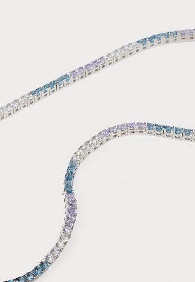 Joyería de tono plateado que presenta un diseño curvado con múltiples filas de piedras preciosas de color azul claro, azul oscuro, lila y transparentes, engastadas en un ajuste con garras.