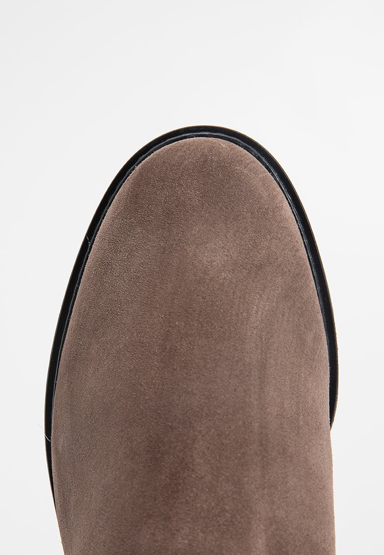 Brauner Wildlederschuh mit schwarzer Sohle, von oben auf einem weißen Hintergrund gezeigt.