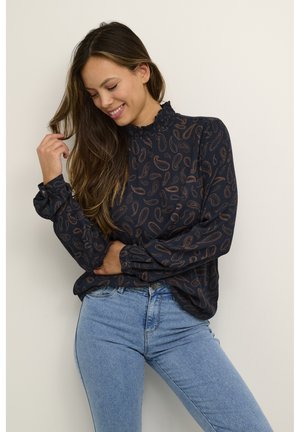 Blouse marine à motif paisley, col montant froncé, manches longues et poignets à boutons, associée à un jean skinny bleu clair.