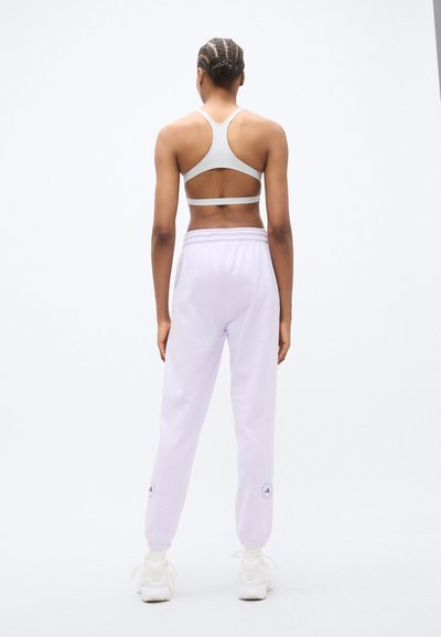 Ανοιχτό μωβ φόρμας με μανσέτες στα πόδια, με ελαστική ζώνη μέσης και λογότυπο, σε συνδυασμό με γκρι αθλητικό σουτιέν. Πλάγια όψη από πίσω.