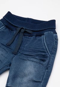 Pantaloni jogger blu navy con vita a costine, coulisse e tasche laterali, con una leggera texture di denim sbiadito.