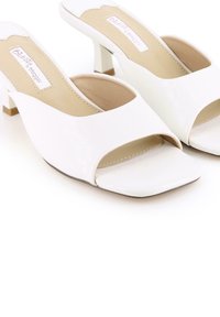 Sandalias blancas de tacón con punta abierta y una textura lisa y brillante. Punta cuadrada, laterales recortados redondeados y un pequeño tacón cuadrado.