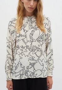 Blusa di colore crema chiaro con un motivo floreale astratto nero, con maniche lunghe e dettagli arricciati ai polsini. Tessuto liscio e testurizzato.