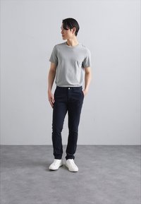 Jasnoszary t-shirt z krótkim rękawem, ciemnonavy spodnie i białe sneakersy. Model stoi na jednolitym tle, prezentując prosty design i dopasowanie.