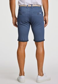 Pantaloni corti blu con un tessuto testurizzato, risvolti, tasche posteriori e una cintura intrecciata, abbinati a sneakers bianche.